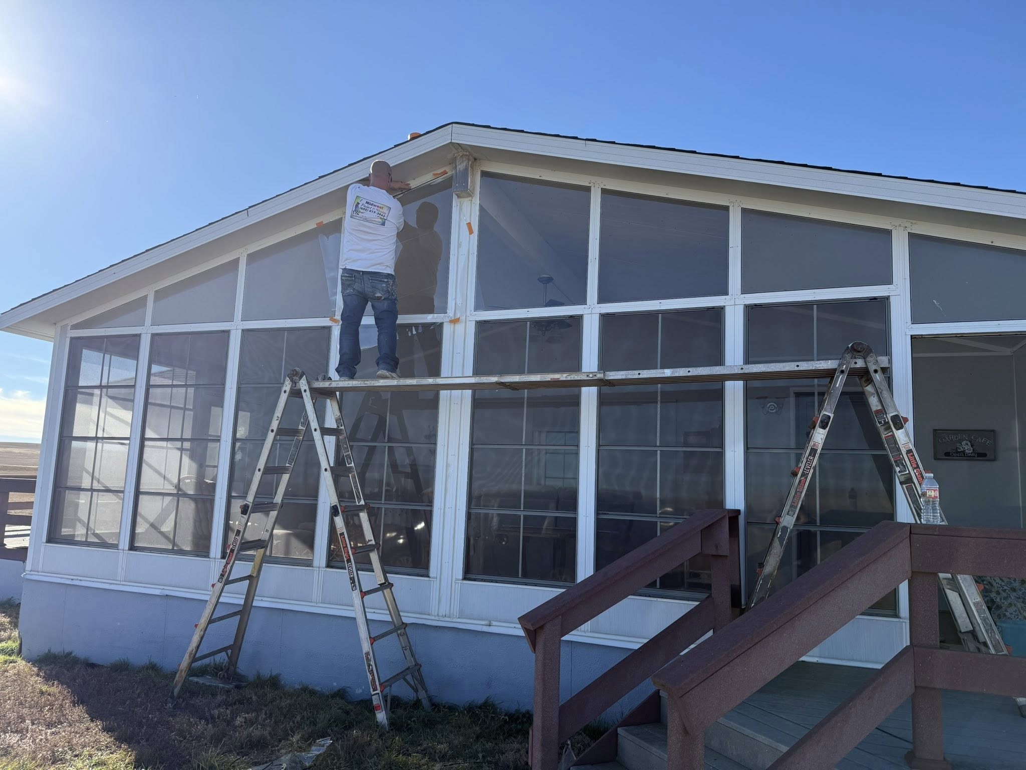 Midwest Paint and Stain crew member on a ladder painting a sunroom's exterior trim