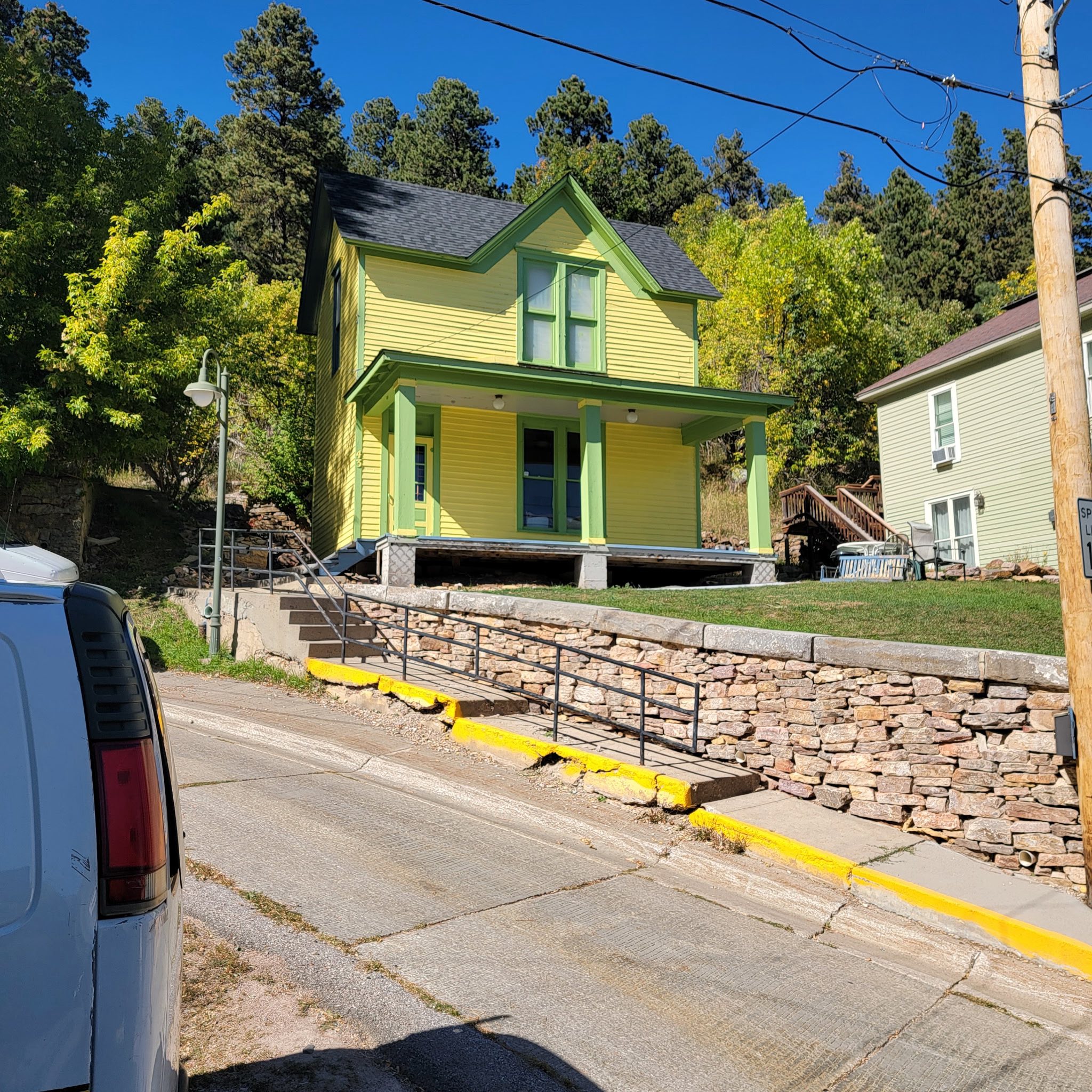 Yellow Victorian two-story home with green trim and a stone retaining wall, repainted in the Black Hills